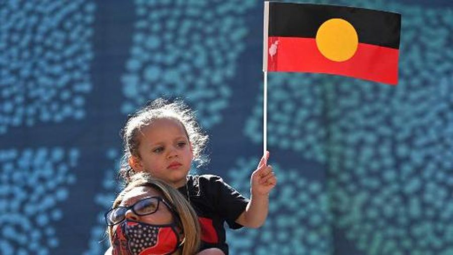 A young girl holds up an Australian Aboriginal flag during an 