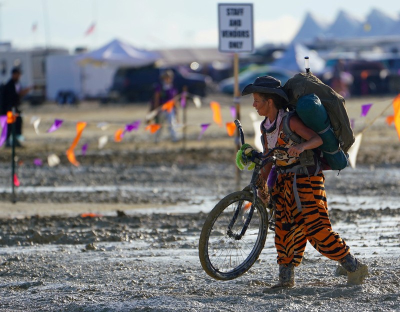 Seorang peserta Burning Man berjalan dengan sepedanya melewati lumpur dekat pintu keluar, setelah hujan badai lebat menyebabkan puluhan ribu orang yang menghadiri festival tahunan terdampar di lumpur di Black Rock City, di gurun Nevada 3 September 2023. (Trevor Hughes/USA Today Network via REUTERS)
