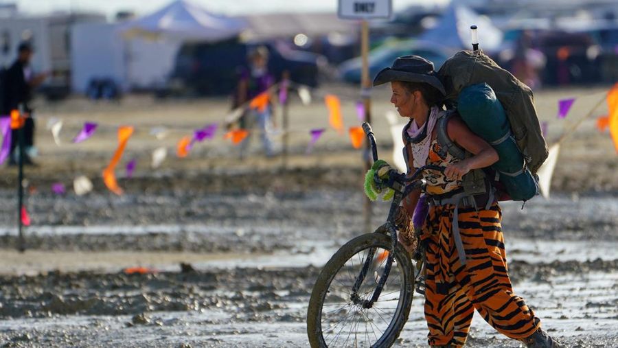 Seorang peserta Burning Man berjalan dengan sepedanya melewati lumpur dekat pintu keluar, setelah hujan badai lebat menyebabkan puluhan ribu orang yang menghadiri festival tahunan terdampar di lumpur di Black Rock City, di gurun Nevada 3 September 2023. (Trevor Hughes/USA Today Network via REUTERS)
