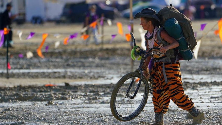 Seorang peserta Burning Man berjalan dengan sepedanya melewati lumpur dekat pintu keluar, setelah hujan badai lebat menyebabkan puluhan ribu orang yang menghadiri festival tahunan terdampar di lumpur di Black Rock City, di gurun Nevada (3/9/2023) waktu setempat. (via REUTERS/TREVOR HUGHES/USA TODAY NETWORK)