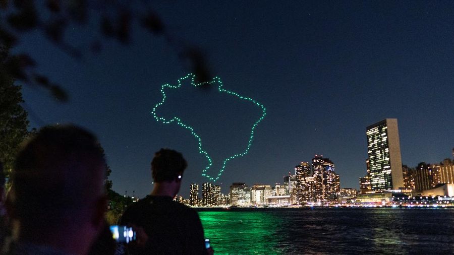 Seorang wanita melihat drone yang membuat tampilan 3-D di luar Markas Besar PBB yang meminta perhatian terhadap hutan hujan Amazon dan perubahan iklim di New York AS, 15 September 2023. (REUTERS/Eduardo Munoz)