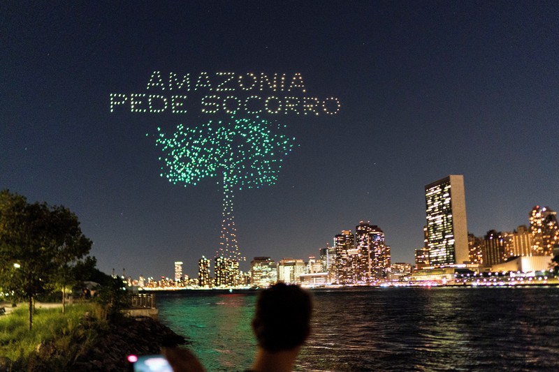 Seorang wanita melihat drone yang membuat tampilan 3-D di luar Markas Besar PBB yang meminta perhatian terhadap hutan hujan Amazon dan perubahan iklim di New York AS, 15 September 2023. (REUTERS/Eduardo Munoz)