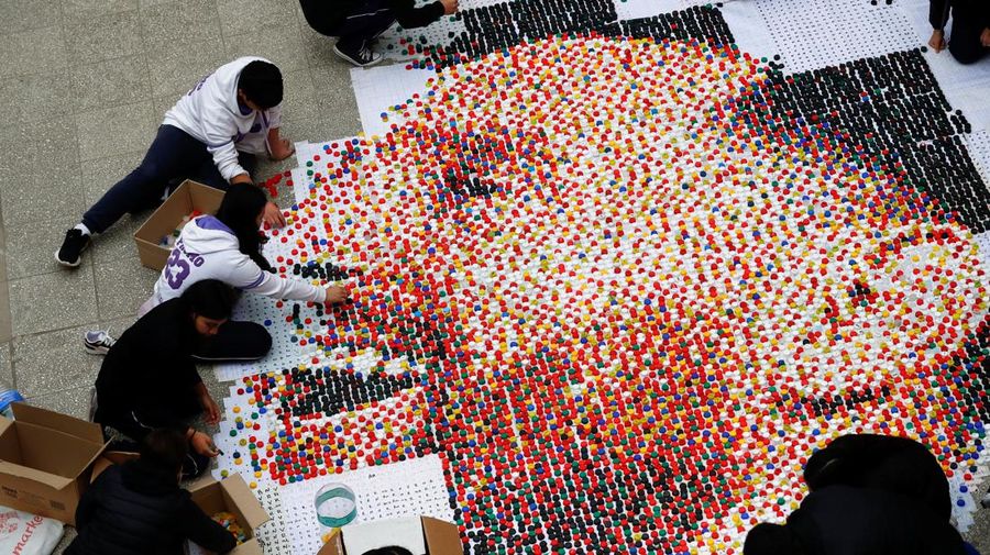 High school students stand next to the mural they made with plastic bottle caps depicting Argentina's soccer superstar Lionel Messi, nine months after Argentina won the soccer World Cup Qatar 2022, in Grand Bourg, on the outskirts of Buenos Aires, Argentina September 19, 2023. REUTERS/Agustin Marcarian