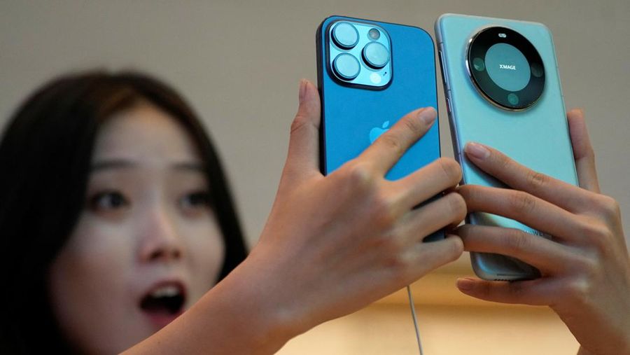A woman looks at a new iPhone 15 Pro and a Huawei Mate 60 Pro as Apple's new iPhone 15 officially goes on sale across China, at an Apple store in Shanghai, China September 22, 2023. REUTERS/Aly Song