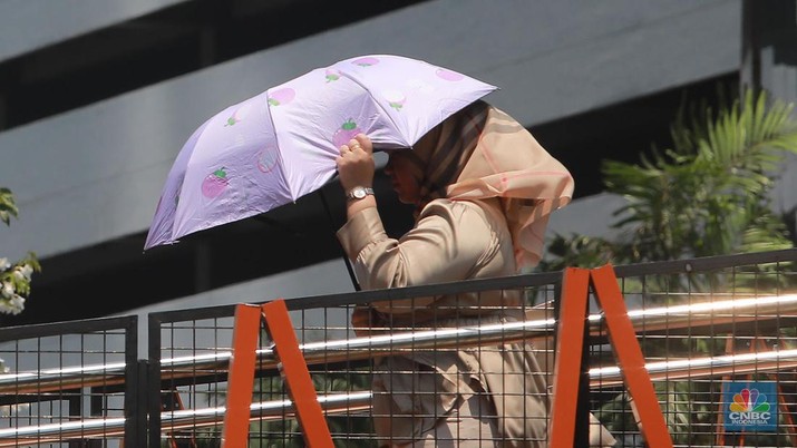 Pejalan kaki menggunakan payung untuk menghindari terik matahari di kawasan Jembatan Pinisi di halte busway Karet, Jakarta, Rabu (27/9/2023). (CNBC Indonesia/Muhammad Sabki)