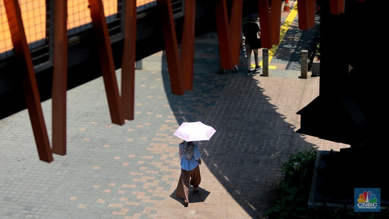 Pejalan kaki menggunakan payung untuk menghindari terik matahari di kawasan Jembatan Pinisi di halte busway Karet, Jakarta, Rabu (27/9/2023). (CNBC Indonesia/Muhammad Sabki)