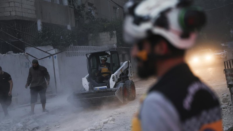 Dalam foto yang disediakan oleh Helm Putih Pertahanan Sipil Suriah, seorang pekerja pertahanan sipil Helm Putih Suriah berlari di lokasi serangan peluru di pinggiran kota utara Jisr al-Shoughour, sebelah barat kota Idlib, Suriah, Kamis , 5 Oktober 2023. Serangan pesawat tak berawak menghantam upacara wisuda perwira militer yang penuh sesak di kota Homs, Suriah pada hari Kamis, menewaskan dan melukai puluhan laporan. Setelah serangan pesawat tak berawak, pemerintah menembaki desa-desa di provinsi Idlib, di bagian barat laut negara yang dikuasai pemberontak. (Syrian Civil Defense White Helmets via AP)