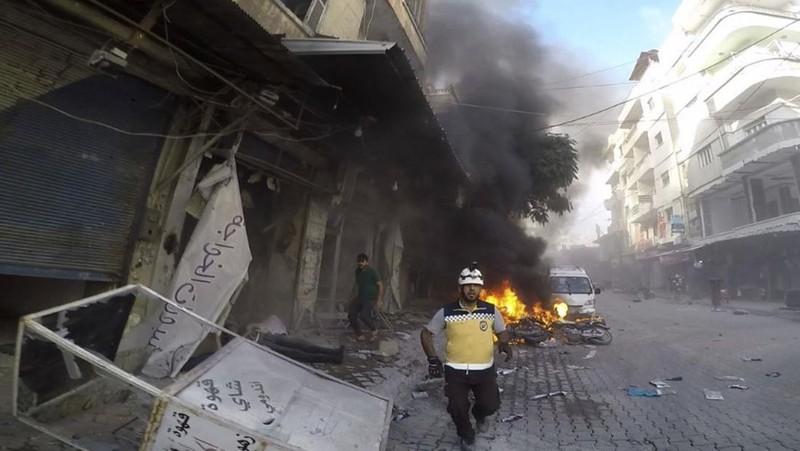 Dalam foto yang disediakan oleh Helm Putih Pertahanan Sipil Suriah, seorang pekerja pertahanan sipil Helm Putih Suriah berlari di lokasi serangan peluru di pinggiran kota utara Jisr al-Shoughour, sebelah barat kota Idlib, Suriah, Kamis , 5 Oktober 2023. Serangan pesawat tak berawak menghantam upacara wisuda perwira militer yang penuh sesak di kota Homs, Suriah pada hari Kamis, menewaskan dan melukai puluhan laporan. Setelah serangan pesawat tak berawak, pemerintah menembaki desa-desa di provinsi Idlib, di bagian barat laut negara yang dikuasai pemberontak. (Syrian Civil Defense White Helmets via AP)