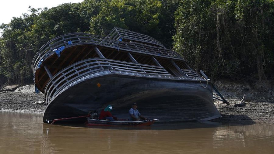 Nelayan berlindung dari terik matahari di samping perahu sungai yang kandas di danau Puraquequara yang mengering di tengah kekeringan parah, di Manaus, negara bagian Amazonas, Brasil, Kamis, 5 Oktober 2023. Hutan hujan Amazon Brasil menghadapi kekeringan parah yang mungkin mempengaruhi sekitar 500.000 orang pada akhir tahun ini. (AP Photo/Edmar Barros)