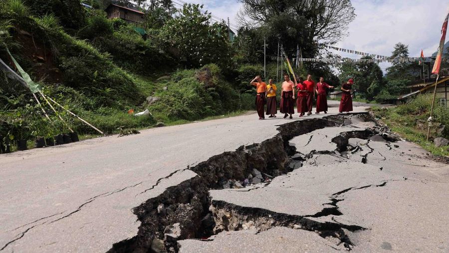 Monks walk along a road with cracks caused by flash floods in Naga-Namgor village, Sikkim, India, October 10, 2023. REUTERS/Francis Mascarenhas