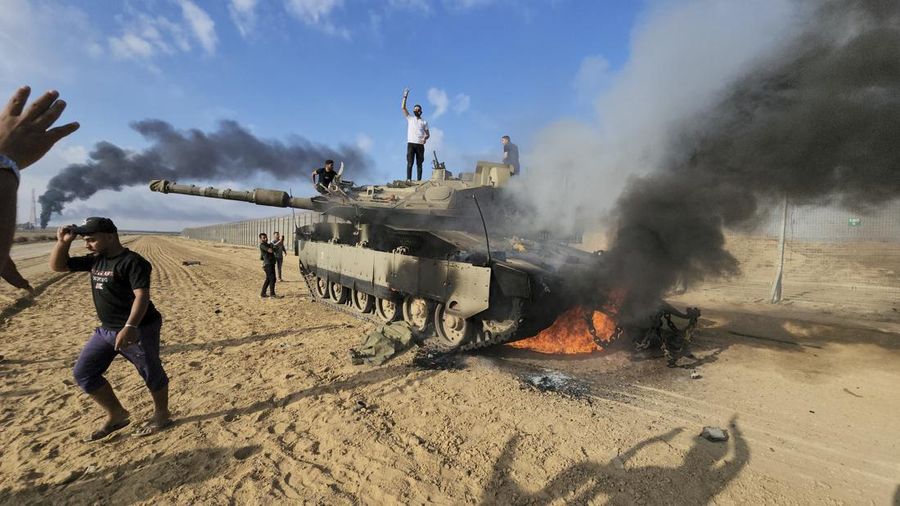 Warga Palestina merayakan dengan tank Israel yang hancur di pagar Jalur Gaza di timur Khan Younis pada Sabtu, 7 Oktober 2023.(AP Photo/Hassan Eslaiah)