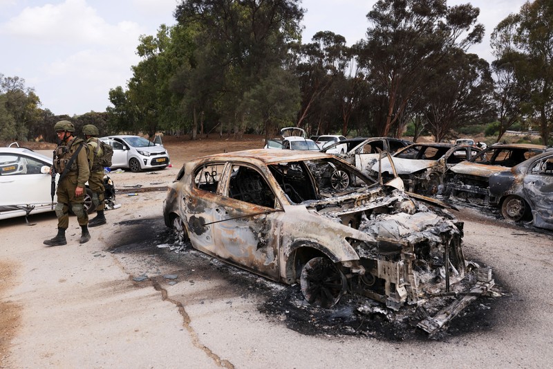 ISRAEL-PALESTINIANS/GAZA Israeli soldiers inspect burnt cars that are abandoned in a carpark near where a festival was held before an attack by Hamas gunmen from Gaza that left at least 260 people dead, by Israel's border with Gaza in southern Israel, October 10, 2023. REUTERS/Ronen Zvulun