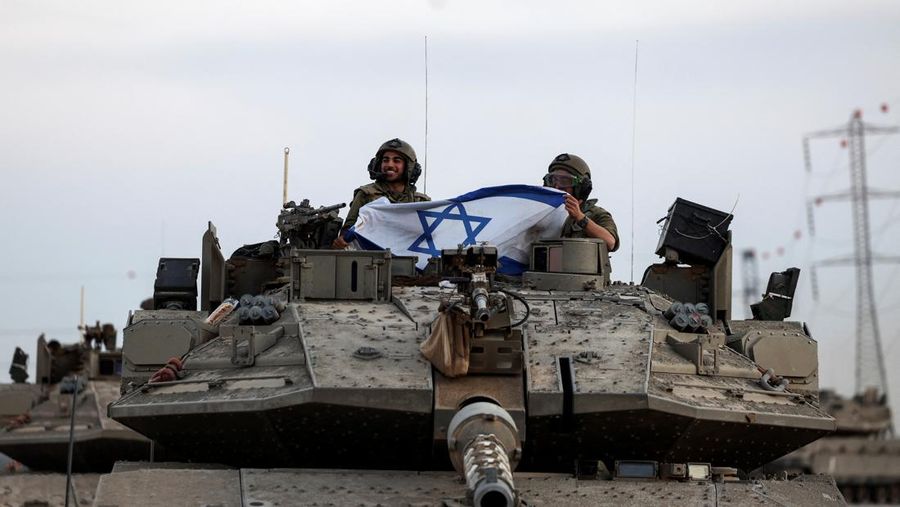 Israeli soldiers hold an Israeli flag while in a tank near Israel's border with the Gaza Strip, in southern Israel, October 12, 2023. REUTERS/Ronen Zvulun