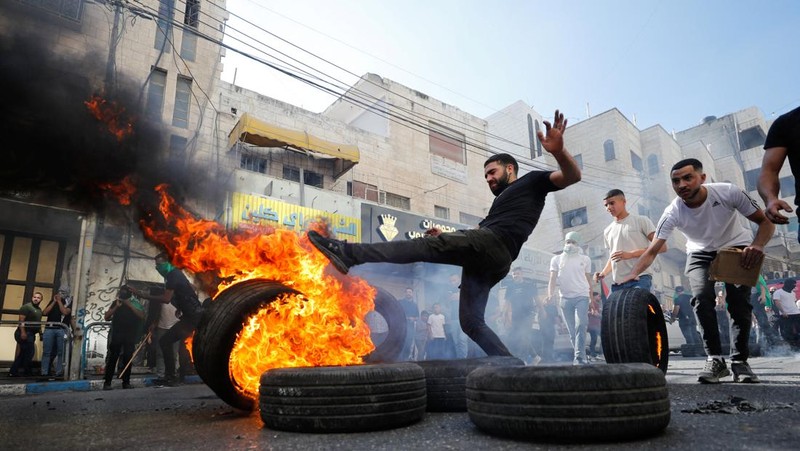Para pengunjuk rasa membakar ban ketika warga Palestina mengambil bagian dalam protes menyusul serangan Israel di Gaza. (REUTERS/Mussa Qawasma)