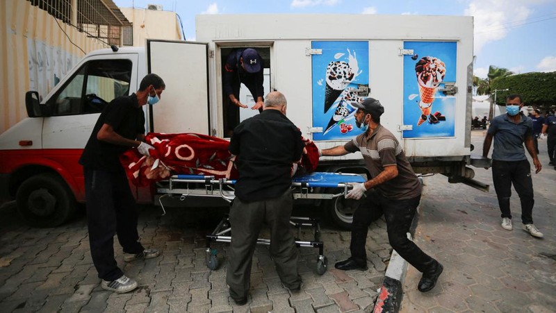 Orang-orang membawa jenazah seorang warga Palestina, yang tewas dalam serangan Israel, dari truk es krim tempatnya disimpan, saat kamar mayat rumah sakit penuh sesak, di tengah konflik Israel-Palestina yang sedang berlangsung, di Jalur Gaza tengah, 15 Oktober 2023. (REUTERS/Stringer)