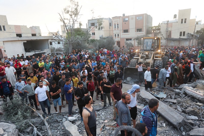 Orang-orang berkumpul saat warga Palestina berupaya mengeluarkan korban dari bawah reruntuhan rumah yang hancur akibat serangan Israel, di Khan Younis di selatan Jalur Gaza 17 Oktober 2023. (REUTERS/Ahmed Zakot)