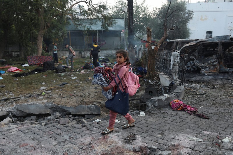 Seorang gadis yang membawa barang-barangnya berjalan di area rumah sakit Al-Ahli di mana ratusan warga Palestina tewas dalam ledakan yang saling menyalahkan oleh pejabat Israel dan Palestina, dan di mana warga Palestina yang meninggalkan rumah mereka berlindung di tengah konflik yang sedang berlangsung dengan Israel, di Kota Gaza, 18 Oktober 2023. (REUTERS/Mohammed Al-Masri)