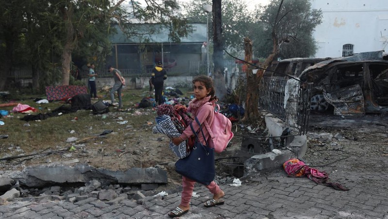 Seorang gadis yang membawa barang-barangnya berjalan di area rumah sakit Al-Ahli di mana ratusan warga Palestina tewas dalam ledakan yang saling menyalahkan oleh pejabat Israel dan Palestina, dan di mana warga Palestina yang meninggalkan rumah mereka berlindung di tengah konflik yang sedang berlangsung dengan Israel, di Kota Gaza, 18 Oktober 2023. (REUTERS/Mohammed Al-Masri)