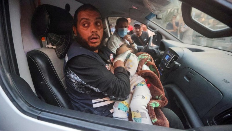 Seorang warga menolong anak yang tertimpa reruntuhan bangunan akibat serangan udara Israel di Jalur Gaza. (REUTERS/Mohammed Salem)
