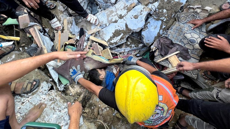 Seorang warga menolong anak yang tertimpa reruntuhan bangunan akibat serangan udara Israel di Jalur Gaza. (REUTERS/Mohammed Salem)