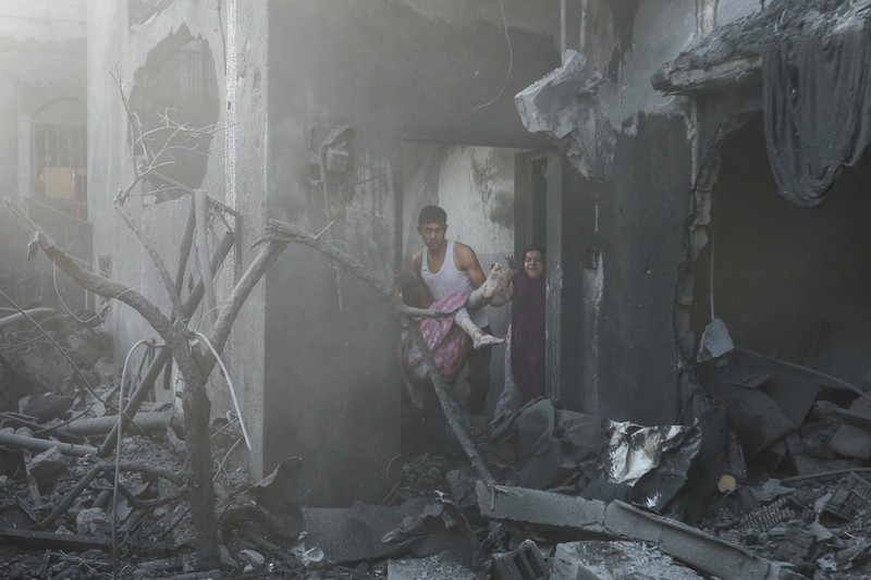 Seorang warga menolong anak yang tertimpa reruntuhan bangunan akibat serangan udara Israel di Jalur Gaza. (REUTERS/Mohammed Salem)