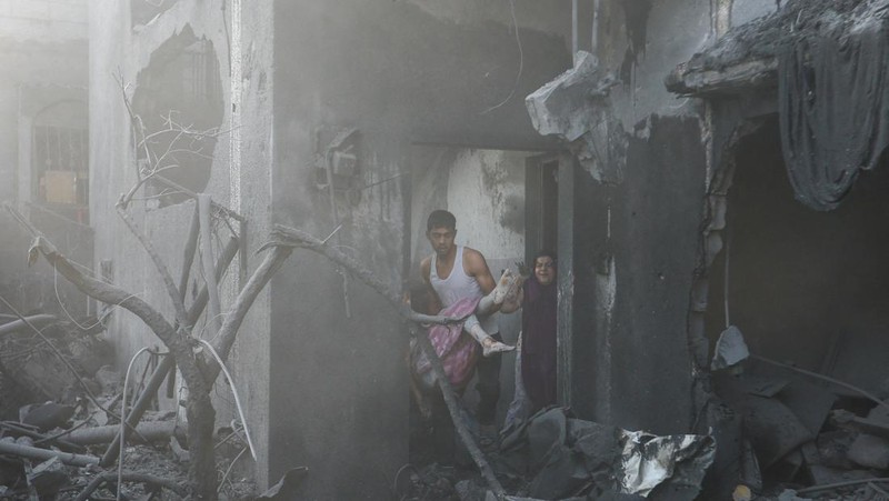 Seorang warga menolong anak yang tertimpa reruntuhan bangunan akibat serangan udara Israel di Jalur Gaza. (REUTERS/Mohammed Salem)
