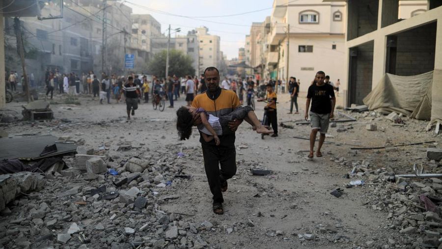 Seorang warga menolong anak yang tertimpa reruntuhan bangunan akibat serangan udara Israel di Jalur Gaza. (REUTERS/Yasser Qudih)