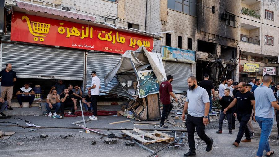 Warga Palestina berjalan di jalan di samping bangunan yang hancur, menyusul serangan Israel di Jenin, di kamp pengungsi Jenin, di Tepi Barat yang diduduki Israel 30 Oktober 2023. (REUTERS/Raneen Sawafta)