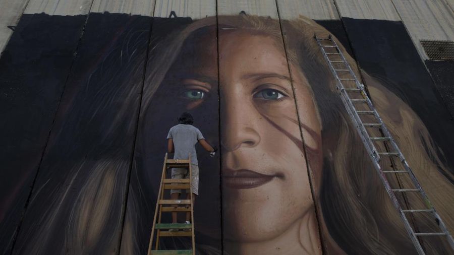 Seorang seniman melukis mural raksasa aktivis terkemuka Palestina Ahed Tamimi di bagian tembok pemisah Israel, di kota Betlehem, Tepi Barat. (AP Photo/Nasser Nasser)