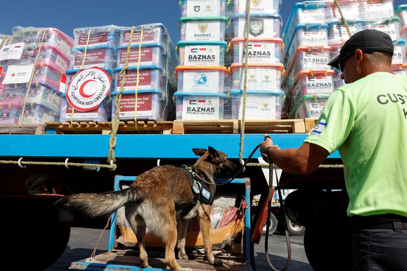 Seorang anggota unit K-9 bea cukai Israel dan seekor anjing memeriksa sebuah truk dengan pasokan kemanusiaan menuju Gaza, di tengah konflik yang sedang berlangsung antara Israel dan kelompok Islam Palestina Hamas, di penyeberangan perbatasan Nitzana di Israel 9 November 2023. (REUTERS/Evelyn Hockstein)