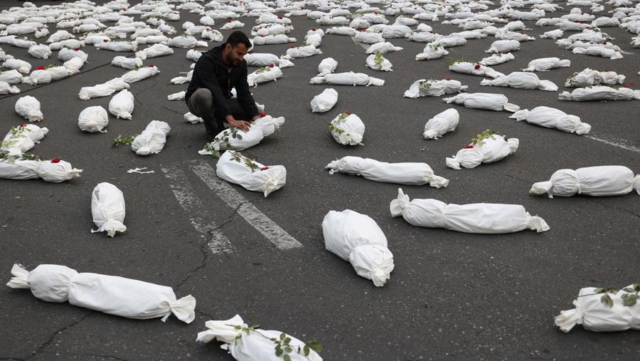 Seorang pria Iran duduk di samping kain kafan simbolis jenazah anak-anak Gaza saat memberi isyarat di sebuah jalan di Teheran, Iran 13 November 2023. (Majid Asgaripour/WANA (West Asia News Agency) via REUTERS)