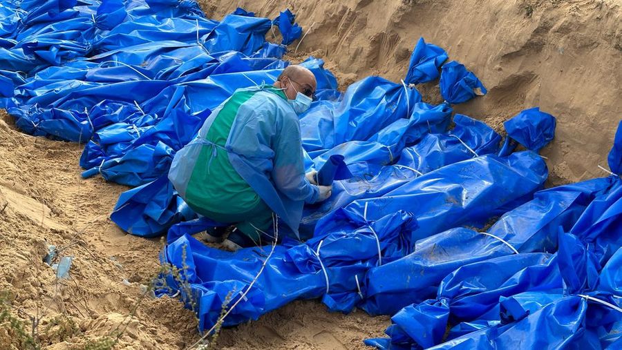 A man arranges the bodies of Palestinians killed in Israeli strikes and fire, as they are buried in a mass grave, after they were transported from Al Shifa hospital in Gaza City for burial, in Khan Younis in the southern Gaza Strip November 22, 2023. REUTERS/Fadi Shana