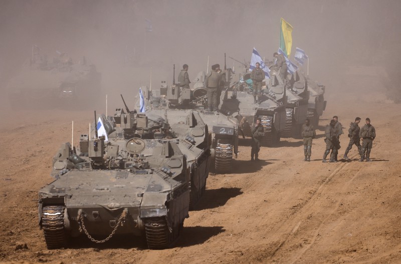ISRAEL-PALESTINIANS/TRUCE Israeli soldiers hold an Israeli flag atop of a military vehicle, near Israel's border after leaving Gaza, during the temporary truce between the Palestinian Islamist group Hamas and Israel, in Israel, November 24, 2023. REUTERS/Amir Cohen