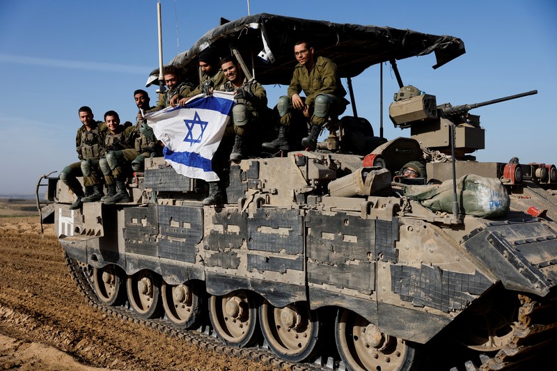 Israeli soldiers hold an Israeli flag atop of a military vehicle, near Israel's border after leaving Gaza, during the temporary truce between the Palestinian Islamist group Hamas and Israel, in Israel, November 24, 2023. REUTERS/Amir Cohen