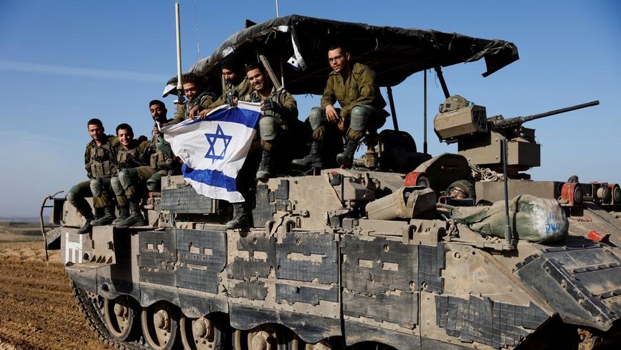 Israeli soldiers hold an Israeli flag atop of a military vehicle, near Israel's border after leaving Gaza, during the temporary truce between the Palestinian Islamist group Hamas and Israel, in Israel, November 24, 2023. REUTERS/Amir Cohen