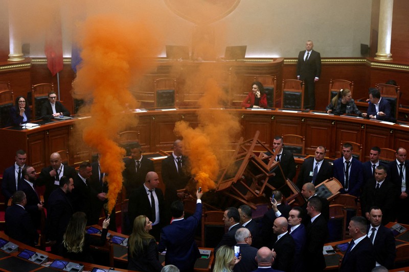 Seorang anggota parlemen dari Partai Demokrat, yang merupakan partaimoposisi terbesar Albania menyalakan bom asap berwarna sebagai tanda protes saat sidang parlemen di Tirana, Albania, Senin (4/12/2023). (REUTERS/Florion Goga)