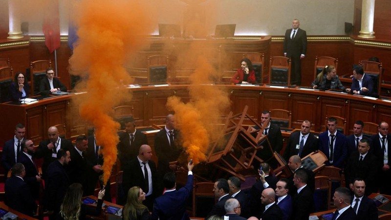Seorang anggota parlemen dari Partai Demokrat, yang merupakan partaimoposisi terbesar Albania menyalakan bom asap berwarna sebagai tanda protes saat sidang parlemen di Tirana, Albania, Senin (4/12/2023). (REUTERS/Florion Goga)