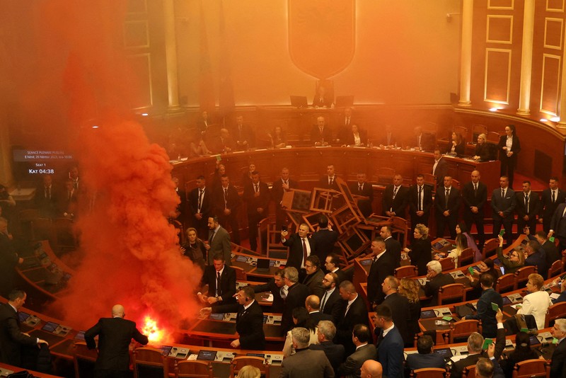 Seorang anggota parlemen dari Partai Demokrat, yang merupakan partaimoposisi terbesar Albania menyalakan bom asap berwarna sebagai tanda protes saat sidang parlemen di Tirana, Albania, Senin (4/12/2023). (REUTERS/Florion Goga)
