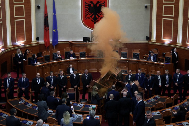 Seorang anggota parlemen dari Partai Demokrat, yang merupakan partaimoposisi terbesar Albania menyalakan bom asap berwarna sebagai tanda protes saat sidang parlemen di Tirana, Albania, Senin (4/12/2023). (REUTERS/Florion Goga)