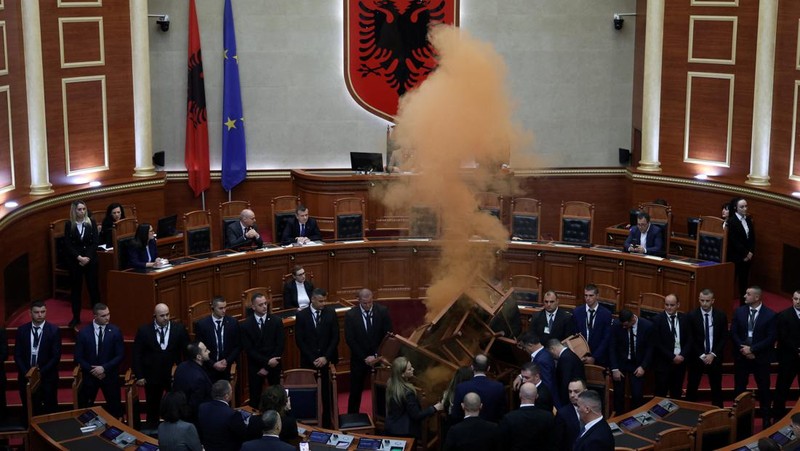 Seorang anggota parlemen dari Partai Demokrat, yang merupakan partaimoposisi terbesar Albania menyalakan bom asap berwarna sebagai tanda protes saat sidang parlemen di Tirana, Albania, Senin (4/12/2023). (REUTERS/Florion Goga)