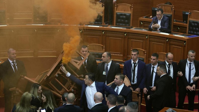 Seorang anggota parlemen dari Partai Demokrat, yang merupakan partaimoposisi terbesar Albania menyalakan bom asap berwarna sebagai tanda protes saat sidang parlemen di Tirana, Albania, Senin (4/12/2023). (REUTERS/Florion Goga)