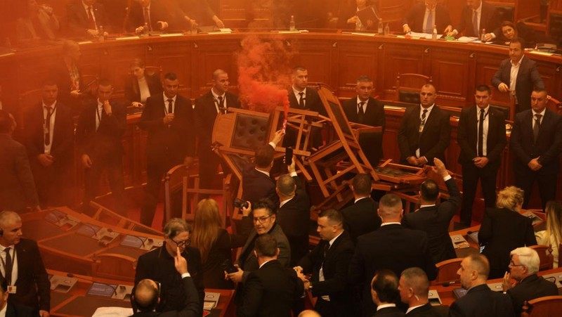 Seorang anggota parlemen dari Partai Demokrat, yang merupakan partaimoposisi terbesar Albania menyalakan bom asap berwarna sebagai tanda protes saat sidang parlemen di Tirana, Albania, Senin (4/12/2023). (REUTERS/Florion Goga)
