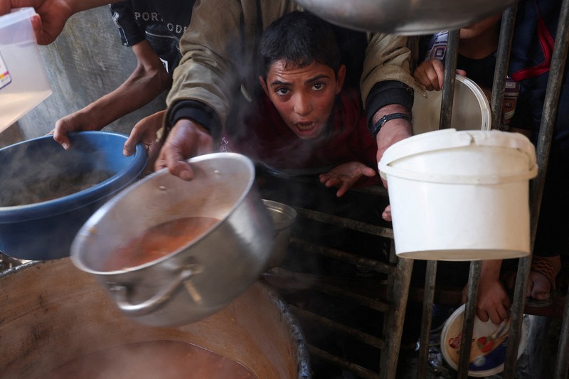 Warga Palestina berebut makanan yang diberikan oleh para sukarelawan, di tengah kekurangan pangan selama konflik antara Israel dan kelompok Islam Palestina Hamas berlanjut, di Rafah, di selatan Jalur Gaza. (REUTERS/Ibraheem Abu Mustafa)