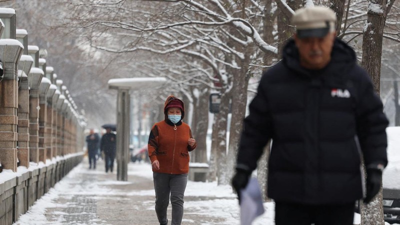 Orang-orang berjalan di jalan di tengah hujan salju di Beijing, Cina 13 Desember 2023. (REUTERS/Tingshu Wang)