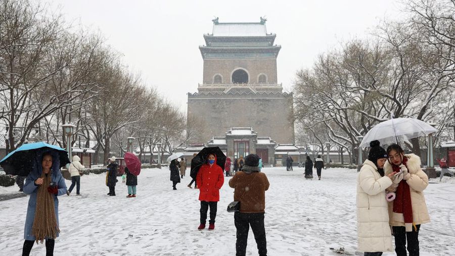 Orang-orang berjalan melewati Menara Lonceng di tengah hujan salju di Beijing, Cina 13 Desember 2023. (REUTERS/Tingshu Wang)