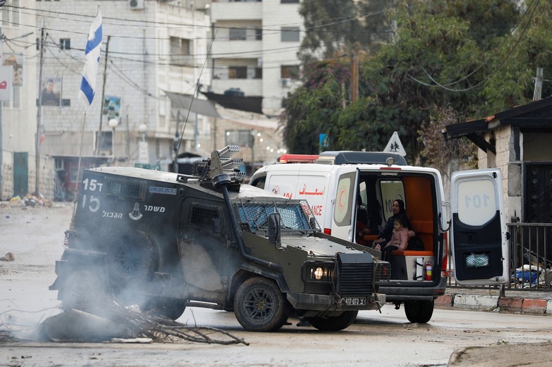 Kendaraan militer Israel memblokir ambulans di jalan selama penggerebekan di Jenin, di tengah konflik yang sedang berlangsung antara Israel dan kelompok Islam Palestina Hamas, di Tepi Barat yang diduduki Israel, 13 Desember 2023. (REUTERS/Raneen Sawafta)