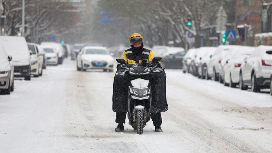 Orang-orang berjalan di jalan di tengah hujan salju di Beijing, Cina 13 Desember 2023. (REUTERS/Tingshu Wang)