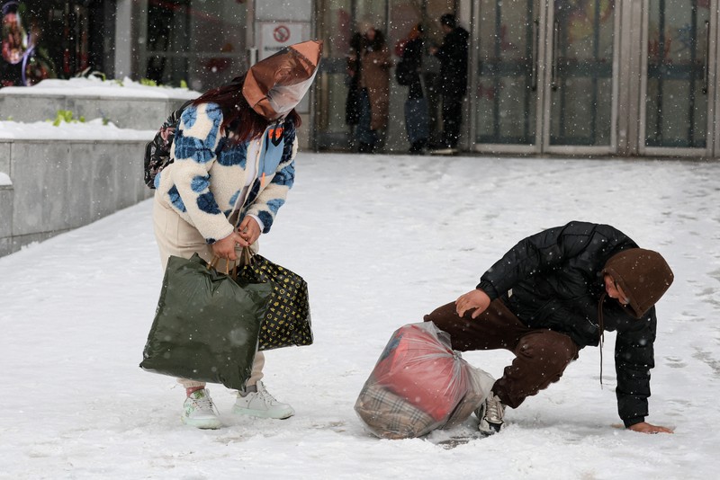 Orang-orang berjalan di jalan di tengah hujan salju di Beijing, Cina 13 Desember 2023. Orang-orang berjalan di jalan di tengah hujan salju di Beijing, Cina 13 Desember 2023. (REUTERS/Tingshu Wang)