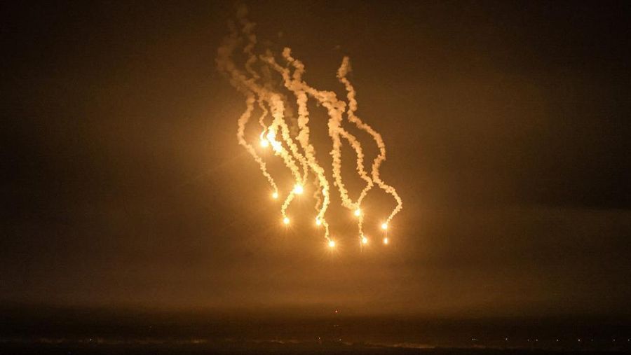 Gambar yang diambil dari Rafah menunjukkan suar menerangi langit di atas Khan Yunis di Jalur Gaza selatan selama serangan Israel, pada 14 Desember 2023, di tengah berlanjutnya pertempuran antara Israel dan kelompok militan Palestina Hamas. Ribuan warga sipil, baik warga Palestina maupun Israel, telah tewas sejak 7 Oktober 2023, setelah militan Hamas Palestina yang berbasis di Jalur Gaza memasuki Israel selatan dalam serangan yang belum pernah terjadi sebelumnya yang memicu perang yang diumumkan oleh Israel terhadap Hamas dengan pemboman balasan di Gaza. (Photo by MAHMUD HAMS / AFP)