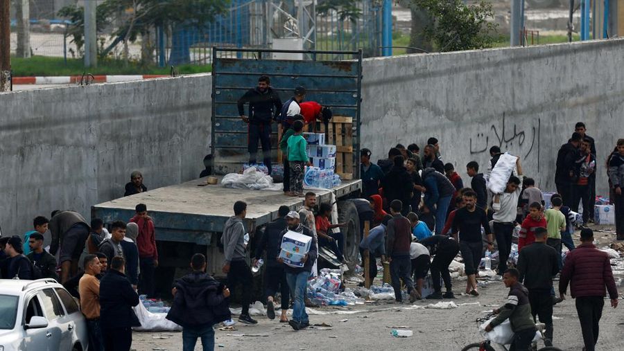 Warga Palestina membongkar kotak berisi botol air dari truk, di tengah kekurangan air minum, saat konflik yang sedang berlangsung antara Israel dan kelompok Islam Palestina Hamas berlanjut, di perbatasan Rafah dengan Mesir, di selatan Jalur Gaza 17 Desember 2023. (REUTERS/Mohammed Salem)